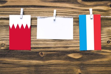 Hanging flags of Bahrain and Luxembourg attached to rope with clothes pins with copy space on white note paper on wooden background.Diplomatic relations between countries.