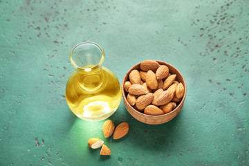 Bowl with almonds and jug of oil on color background