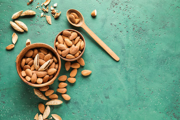 Bowls with tasty almonds on color background