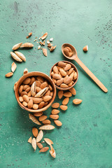 Bowls with tasty almonds on color background