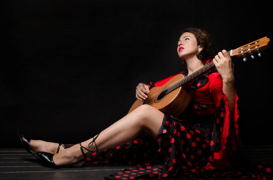 Carmen beautiful woman in red dress, with guitar on dark background sitting on the floor