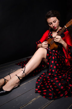 Carmen beautiful woman in red dress, with guitar on dark background sitting on the floor