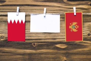 Hanging flags of Bahrain and Montenegro attached to rope with clothes pins with copy space on white note paper on wooden background.Diplomatic relations between countries.