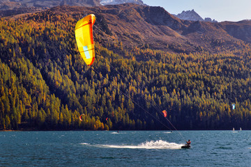 Mountain landscape with a lot of kite surfers and windsurfers moving in a lake.