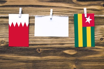 Hanging flags of Bahrain and Togo attached to rope with clothes pins with copy space on white note paper on wooden background.Diplomatic relations between countries.