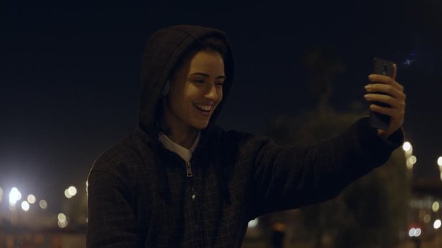 Beautiful Female Listening To Music on Wireless Headphones takes a selfie on city skate Park wearing a sweatshirt hoodie