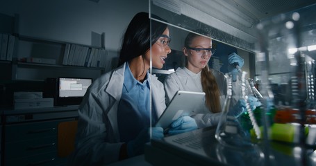 Portrait of two female scientists are analyzing with a pipette a liquid to extract the DNA and molecules in the test tubes in laboratory. 