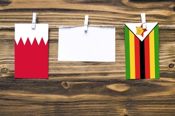 Hanging flags of Bahrain and Zimbabwe attached to rope with clothes pins with copy space on white note paper on wooden background.Diplomatic relations between countries.