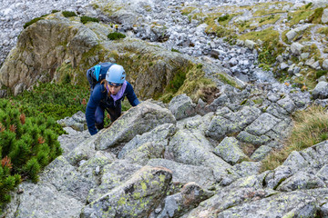 A young girl with a backpack and a helmet climbs the rocky terrain in the mountains.