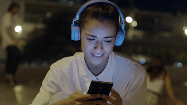 Beautiful Female Listening To Music on Wireless Headphones dancing During Training In city skate Park