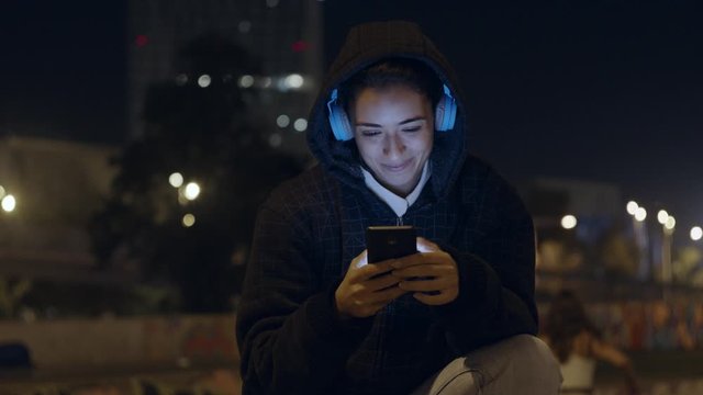 Beautiful Female Listening To Music on Wireless Headphones takes a selfie on city skate Park wearing a sweatshirt hoodie