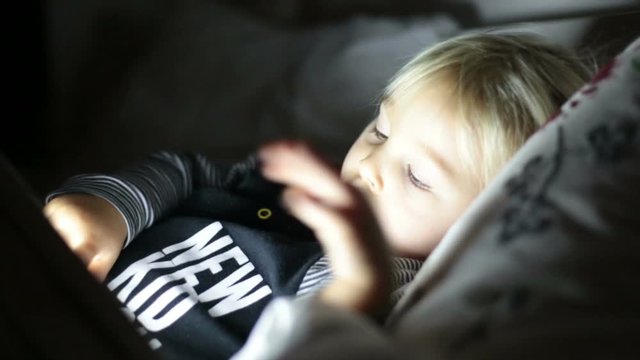 Happy toddler boy watching nights story tale at night on tablet in ebd