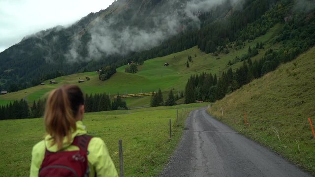 Woman hiking down dirt road in Grindelwald Switzerland as train passes
