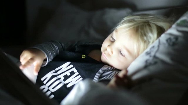 Happy toddler boy watching nights story tale at night on tablet in ebd