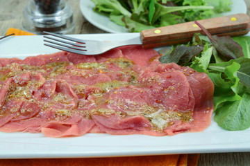 beef carpaccio on a plate, accompanied by salad
