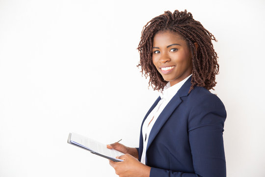 Happy new employee studying job instructions, holding documents, looking at camera. Young African American business woman standing isolated over white background. Career beginning concept