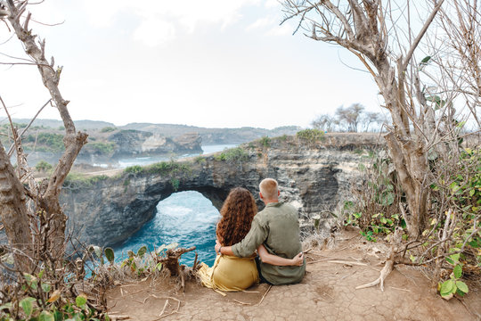 Man and woman in honeymoon near Broken Beach in Nusa Penida, Couple sitting n the cliff with view on roken beach, popular travel destinatio from Bali