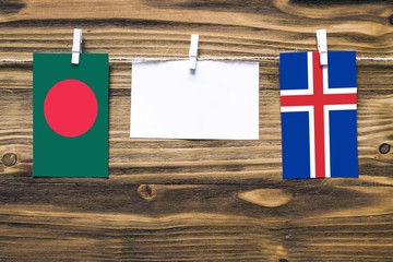 Hanging flags of Bangladesh and Iceland attached to rope with clothes pins with copy space on white note paper on wooden background.Diplomatic relations between countries.