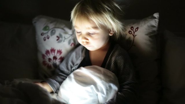 Happy toddler boy watching nights story tale at night on tablet in ebd