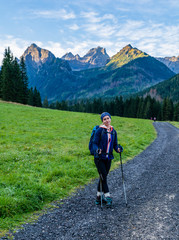 Young woman (tourist) with trekking poles on the trail in the valley. In the background beautiful peaks lit by the morning sun. Tatra Mountains. Slovakia.