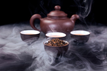 Asian tea ceremony. Clay teapot and tea cups with vapor on a black background.