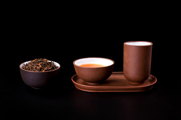 Asian tea ceremony. Clay tea cups and tea drink with dry tea leaves isolated on a black background.