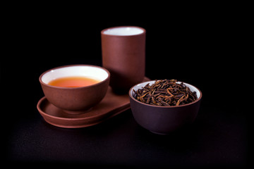 Obraz na płótnie Canvas Asian tea ceremony. Clay tea cups with dry tea leaves and tea drink on a black background.