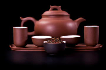 Asian tea ceremony. Clay teapot and tea cups with dry tea leaves on a black background.
