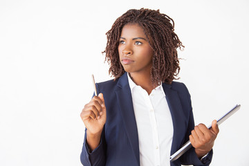 Pensive female job applicant filling up job application, holding pen and folder, looking up. Young...