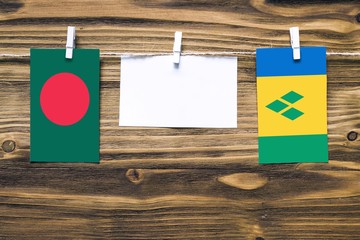 Hanging flags of Bangladesh and Saint Vincent And The Grenadines attached to rope with clothes pins with copy space on white note paper on wooden background.Diplomatic relations between countries.