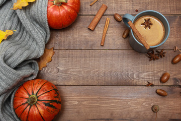 Grey cup of coffee with milk and spices, scarf, yellow oak leaves, acorns, orange pumpkins on dark brown wooden table. Autumn drink concept. Fall, pumpkin spicy latte, thanksgiving, top, copy space