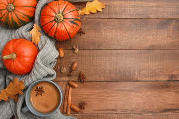 Grey mug of coffee with milk and spices, scarf, yellow oak leaves, orange pumpkins on dark brown wooden table. Autumn drink concept. Fall, pumpkin spicy latte, thanksgiving, top, copy space