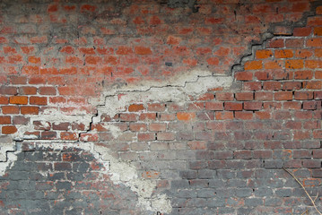 Old damaged stained brick wall with big cracks and splashes of black paint