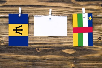 Hanging flags of Barbados and Central African Republic attached to rope with clothes pins with copy space on white note paper on wooden background.Diplomatic relations between countries.