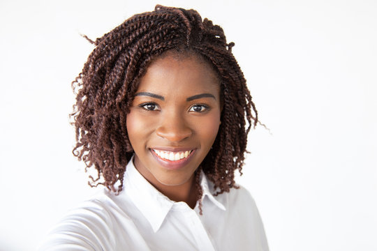 Selfie of happy joyful female professional, wearing white shirt, looking at camera and smiling. Young African American business woman standing isolated over white background. Closeup portrait concept