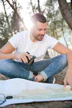 Hombre joven y atractivo ojeando un mapa de viajes para emprender una ruta en medio del bosque.