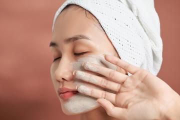 Beautiful cheerful Asian teen girl applying facial clay mask. Beauty treatments, isolated on light...