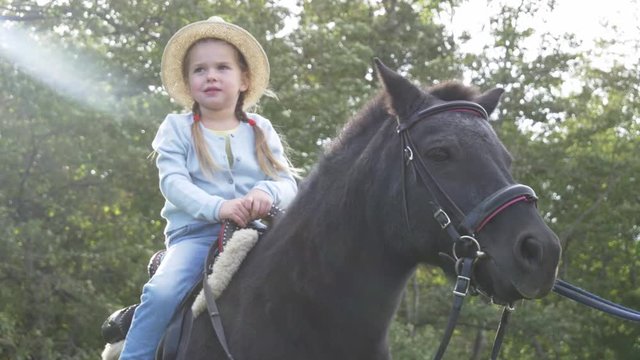 Little girl riding black pony in park