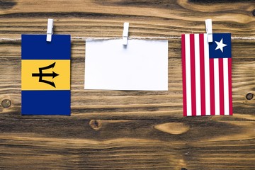 Hanging flags of Barbados and Liberia attached to rope with clothes pins with copy space on white note paper on wooden background.Diplomatic relations between countries.
