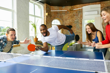 Young people playing table tennis in workplace, having fun. Friends in casual clothes play ping...
