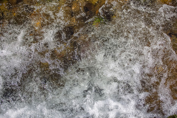View of small waterfall on river with detail of water foam, rocks and river vegetation