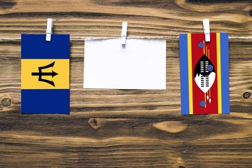 Hanging flags of Barbados and Swaziland attached to rope with clothes pins with copy space on white note paper on wooden background.Diplomatic relations between countries.