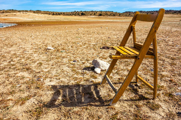 Obraz na płótnie Canvas Broken wooden chair on the shore of a beach or a reservoir with a cloudy blue sky in the background