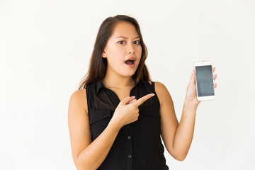 Shocked woman pointing at smartphone with blank screen. Surprised young woman with open mouth holding cell phone with blank screen and looking at camera. Advertising concept