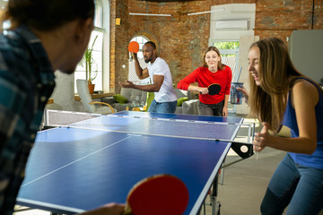 Young people playing table tennis in workplace, having fun. Friends in casual clothes play ping...