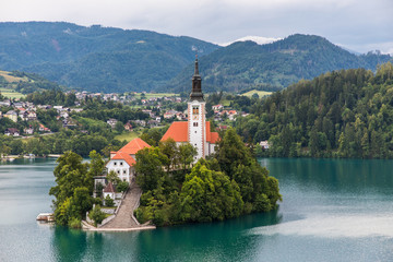 Fototapeta na wymiar Bled, Slovenia - July, 2019: Lake Bled with St. Marys Church of Assumption on small island. Mountains and valley on background. Space for your text.