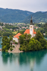 Fototapeta na wymiar Bled, Slovenia - July, 2019: Lake Bled with St. Marys Church of Assumption on small island. Mountains and valley on background. Space for your text.