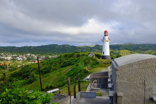 A lighthouse on top of a lush green hill overlooking a small town and the mountains. Basco, Batanes, Philippines