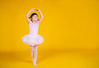 Portrait of little asian child girl dreams of becoming ballerina in a pink tutu skirt isolated on yellow background. Happy young girl practise her dance. Education childhood toddler lifestyle concept © paulaphoto