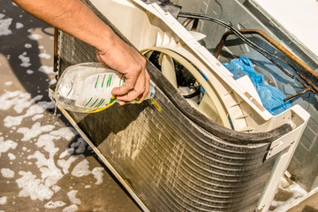 a professional electrician is cleaning the window air conditioner on the roof top of a house with his high pressure water gun   